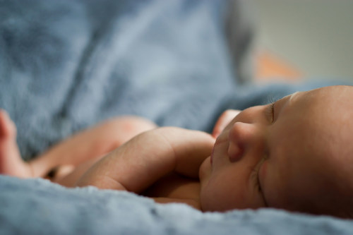 Newborn baby sleeping on a soft blue blanket, with a peaceful expression and delicate features.